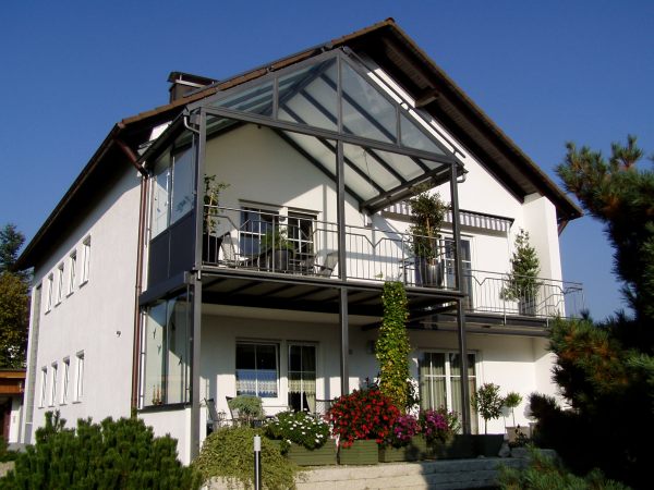 Balkonanbau mit verglaster Überdachung, seitlichem Windschutz, Sonnenrollo, Geländer              mit Edelstahlhandlauf