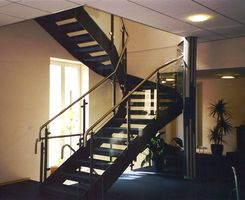 Stahltreppe, Stufen mit Teppich belegt, Geländer mit Glassegmente und Edelstahlhandlauf